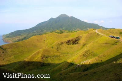 Volcano backdrop and cars on top of rolling hills of Batanes